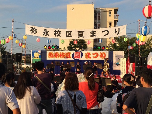 弥永校区夏祭りにステージの上で音楽を演奏する人たちとそれを眺める観客の写真