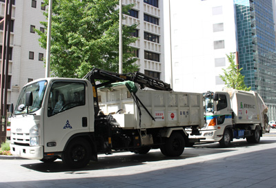 久留米市に対する災害廃棄物の収集支援に向かうクレーン付きトラックとパッカー車（ごみ収集車）の写真
