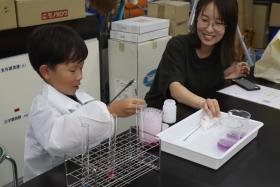 参加者の親子が、重曹やクエン酸などを使った実験で発生した大量の泡がビーカーからあふれ出す様子を楽しみながら観察している様子