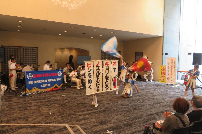 曲に合わせて消火器の使い方を説明する福岡市消防カラーガード隊の写真