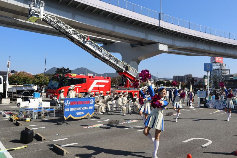 消防車を背にして演奏と演技を行う福岡市消防音楽隊の写真