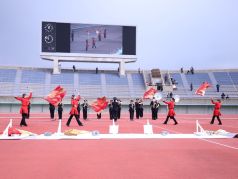 陸上競技場内で演奏と演技を行う福岡市消防音楽隊の写真