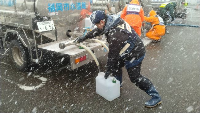 吹雪の中、給水車から水を給水する水道局職員