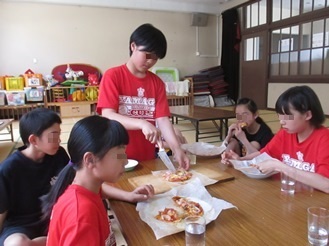 ピザを切る上級生と、ピザを食べる子どもたちの写真