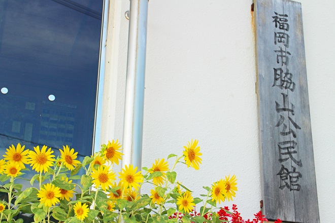 下にヒマワリがたくさん咲いていて右側に脇山公民館の看板が見える写真