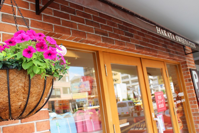 左に濃いピンクの花がたくさん咲いたハンギングバスケットが見える店舗入り口の写真