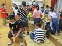 子ども達が作った段ボールベッドに、自治協木村会長も一緒に座ってみました。