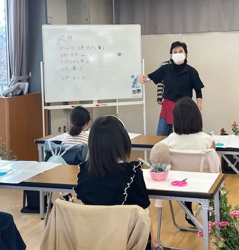 フラワーアレンジメントの説明をする講師と、聞き入る小学生