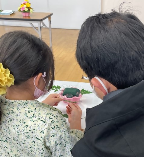 作業をする子どもと、横で見守る親の後ろ姿