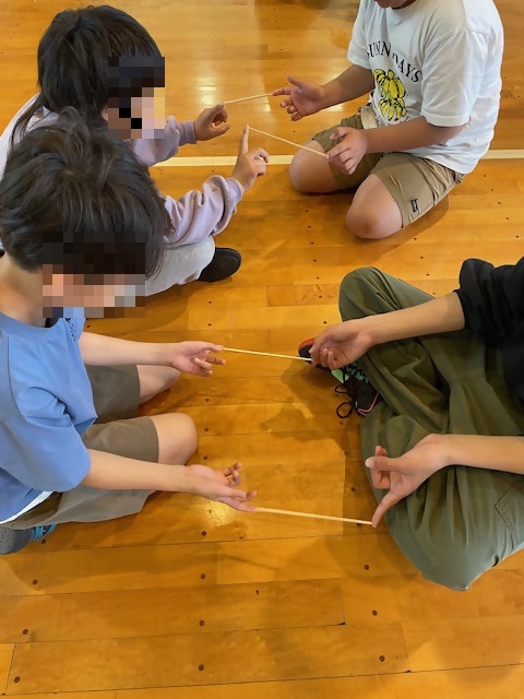 二人で向かい合い指一本で割りばしをはさみ立ったり座ったり