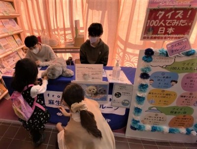 子どもが学生の出すクイズに答えながら、机の上のぬいぐるみに触れている写真