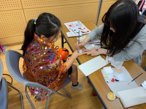 専門学生が子どもの右手の甲にお化けのイラストを描いている写真