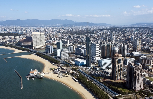 福岡の街並み。海辺の福岡タワーやドームを中心に、奥にはビル群と山々が広がっている。