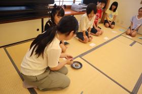 学生のサポートを受けながら、お菓子を懐紙に移す参加者の様子