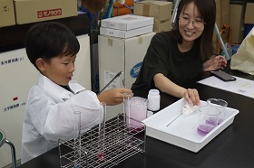 参加者の親子が、重曹やクエン酸などを使った実験で発生した大量の泡がビーカーからあふれ出す様子を楽しみながら観察している様子