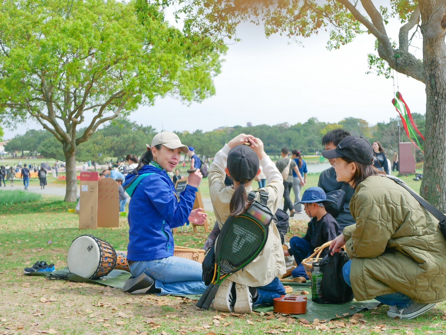 あそび場サポーターとともに、屋外で太鼓などの音楽あそびをする子どもと保護者