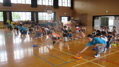 大人が子どもたちの見本でカローリングを投じている様子