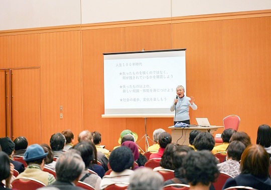 過去のイベントの様子「スクリーン付きの会場で、たくさんの人の前でお話しする若宮正子さん」