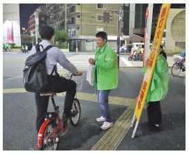 自転車利用者に啓発グッズやチラシを配布し、ライトの点灯や安全運転への協力を呼び掛けている写真