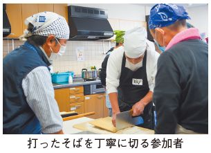 打ったそばを丁寧に切る参加者の写真