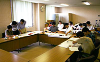 写真：会議室で机に古文書を広げて調査・整理にあたる10数人の委員や調査補助員のアルバイトたち