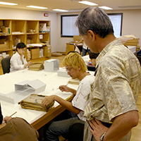 福岡市総合図書館における近現代専門部会の調査風景　同館の一室で近代文書を整理する調査補助員の学生たちと有馬部会長