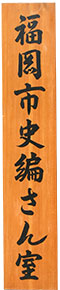 写真：板木に「福岡市史編さん室」と墨で書かれた看板。実物は縦1メートル、横20センチメートルほどの大きさである