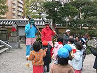 写真：東長寺の境内で、節分祭が行われている様子。留学生2人が扮する赤鬼と青鬼が、子供たちに囲まれている。鬼2人はそれぞれ赤と青の鬼面を被り、黒い金棒を持っている