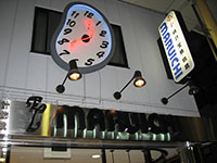 写真：唐人町商店街の時計店の看板を写したもの。夜の撮影。「EL MARUICHI」と書かれた看板の横に、歪んだ時計のモニュメントが掛かっている