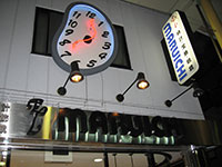 写真:唐人町商店街の時計店の看板を写したもの。夜の撮影。「EL MARUICHI」と書かれた看板の横に、歪んだ時計のモニュメントが掛かっている
