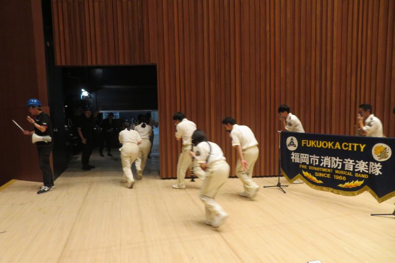 福岡市民ホール大ホールの舞台上から避難訓練をする福岡市消防音楽隊の写真